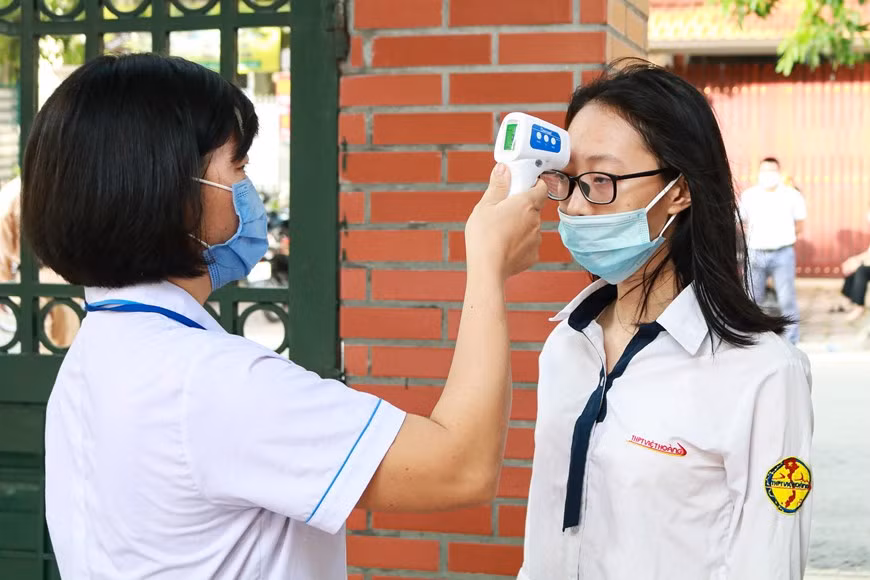 Trước khi bước vào phòng thi dự môn Ngữ Văn, thí sinh được kiểm tra y tế nghiêm ngặt như đo thân nhiệt, đeo khẩu trang và rửa tay bằng dung dịch sát khuẩn. (Ảnh: Nguyên An/Vietnam+)