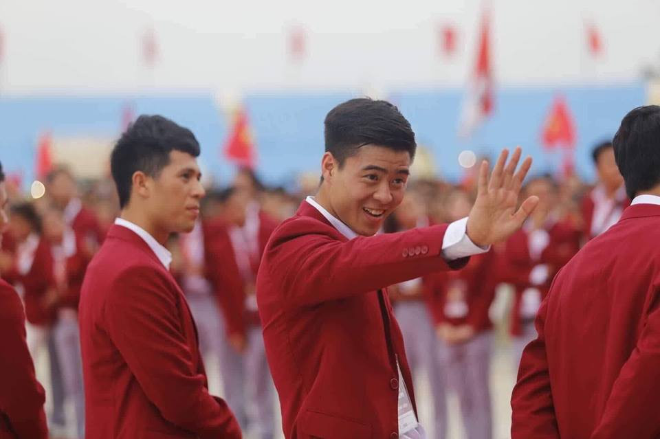 Anh chàng trung vệ mặc áo vest đỏ tươi cười chào người hâm mộ.