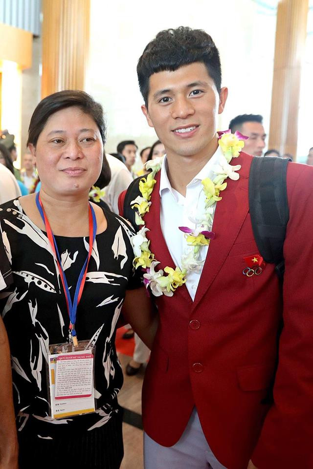 Trần Đình Trọng mặc sơ mi trắng và vest đỏ chững chạc chụp ảnh cùng mẹ.