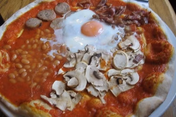 Pizza “thập cẩm” English Breakfast, Anh: Đầy đủ thành phần của một bữa sáng kiểu Anh với xúc xích Anh, đậu nướng, trứng chiên, thịt xông khói, khoai tây, nấm, cà chua... đều xuất hiện trên bề mặt của chiếc bánh pizza. Ảnh: Internet.