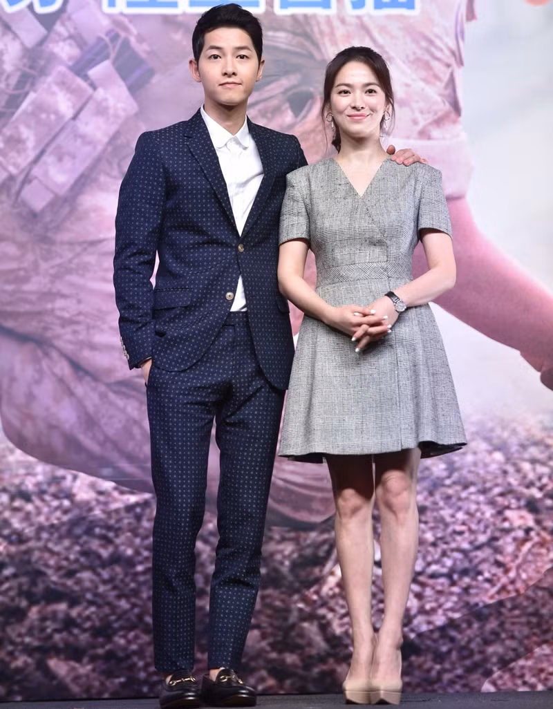 Song Joong Ki bảnh bao với vest đen họa tiết nhỏ, còn bạn gái anh đơn giản, thanh lịch trong bộ váy xòe xẻ cổ chữ V.