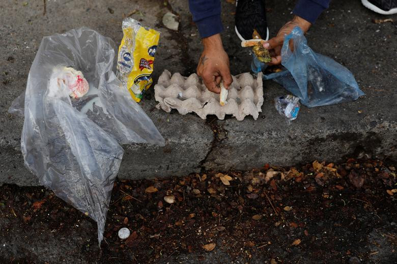 Một nhân viên bảo vệ nhặt thức ăn thừa cạnh thùng rác ở thủ đô Venezuela ngày 27/2.