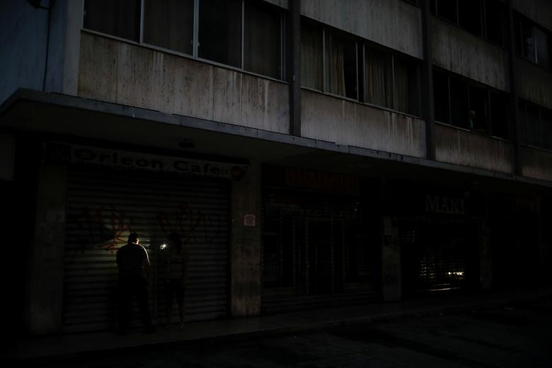 Một người dân bật đèn điện thoại để thắp sáng khi đóng cửa hàng trong đợt mất điện ở thủ đô Venezuela hồi tuần trước.