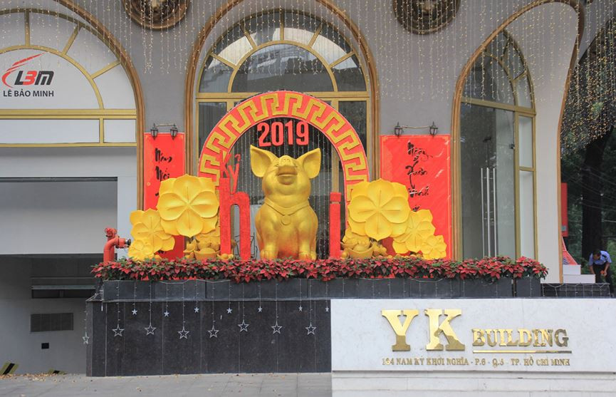 Phía trước một tòa nhà ở quận 3 trang trí khung cảnh chơi Tết với chú heo vàng cạnh những đóa hoa mai và đôi câu đối.