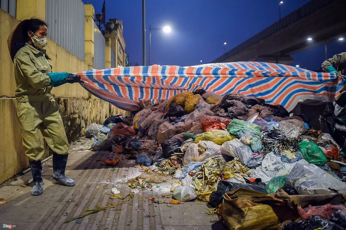 Công nhân vệ sinh môi trường phải dùng nhiều tấm bạt cỡ lớn để phủ lên bãi rác tự phát trên đường Nguyễn Quý Đức.
