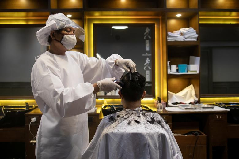 Thợ cắt tóc mặc đồ bảo hộ và đeo khẩu trang cẩn thận khi cắt tóc cho khách hàng ở thành phố Mandaluyong, Manila, Philippines, ngày 8/6.