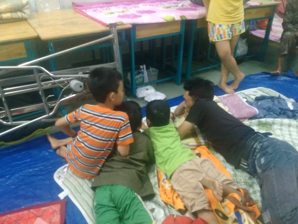 Người đàn ông cùng các cháu nhỏ nằm trên tấm bạt vui vẻ cùng nhau xem phim qua điện thoại. 