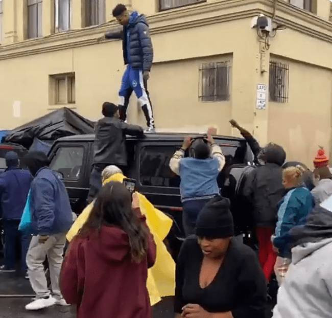 Blueface rút tập tiền ra rồi tung lên trời. Nhiều người xô đẩy nhau để nhặt được càng nhiều tiền càng tốt.