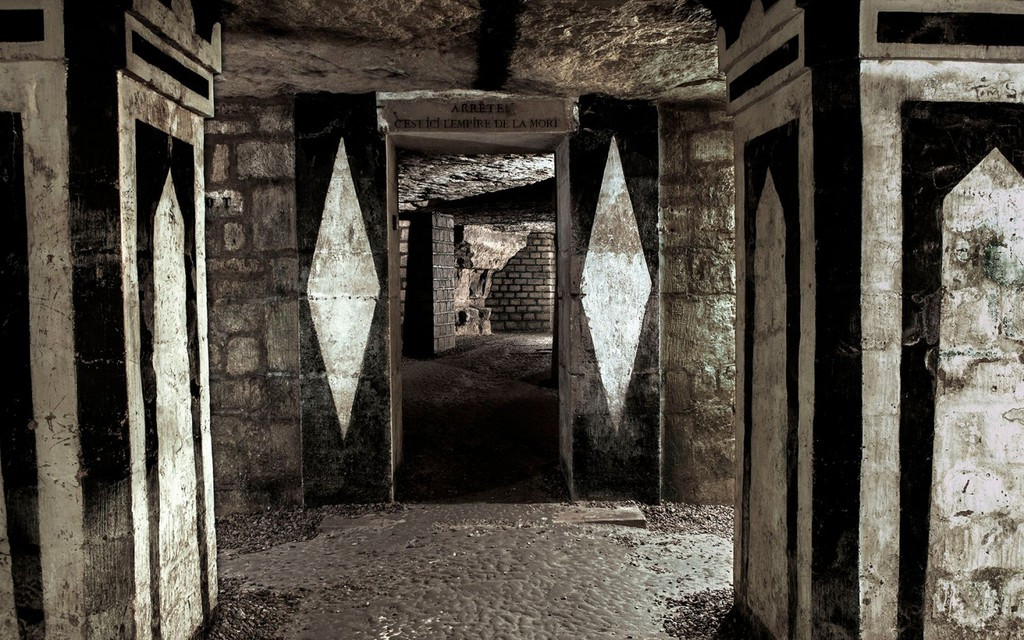 Ngay lối vào, một khoảng trống được dành cho các triển lãm theo chủ đề. Tiếp đó là một cánh cửa với dòng chữ: "Arrête, c'est ici l'empire de la mort!" (Dừng lại! Đây là vương quốc của tử thần!). Ảnh: Lescatacombs.