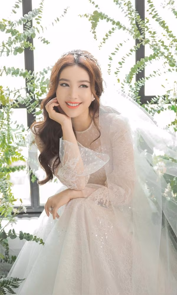 Thiết kế đầu tiên có phần cổ kín đáo, phần chân váy xòe bồng bềnh. Cô chọn kiểu trang điểm nhẹ nhàng, tóc xoăn lơi và đầu cài phụ kiện tinh tế.