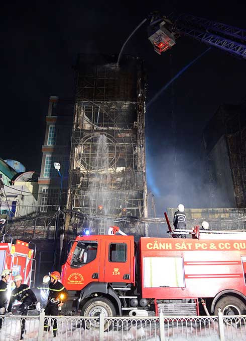 Dù lửa đã tắt nhưng lực lượng cứu hỏa vẫn đang tiếp tục phun nước. Có thể thấy là quán Karaoke cháy chỉ còn trơ khung. Ảnh: Tuổi Trẻ