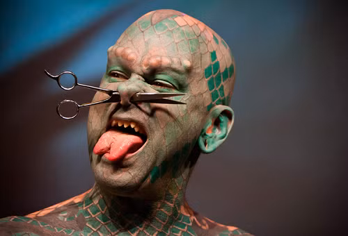 Trẻ con sẽ khóc thét khi chứng kiến người đàn ông với lớp da xăm xanh đỏ như rắn, lưỡi chẻ, u sần vùng lông mày cùng tạo hình chiếc khuyên là một cái kéo.