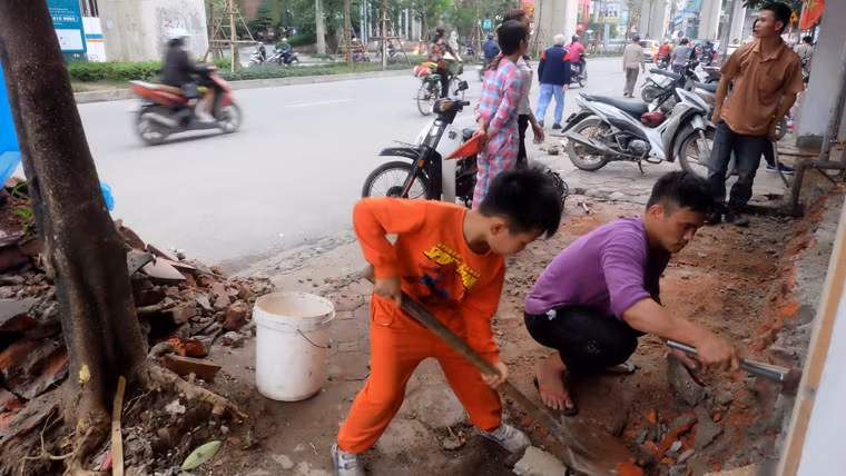 Rất nhiều người cùng nhau đập gạch, đá, vôi vữa nham nhở trên vỉa hè. Một cậu bé cũng hăng hái giúp đỡ mọi người dọn dẹp.