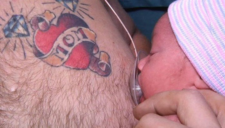 Em bé mới sinh bú lấy bú để từ ti nhân tạo gắn trên ngực cha mình.