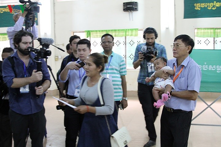 Một cán bộ hỗ trợ bà mẹ có con nhỏ đi bầu cử.