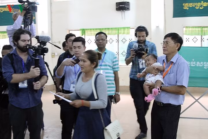 Một cán bộ hỗ trợ bà mẹ có con nhỏ đi bầu cử.