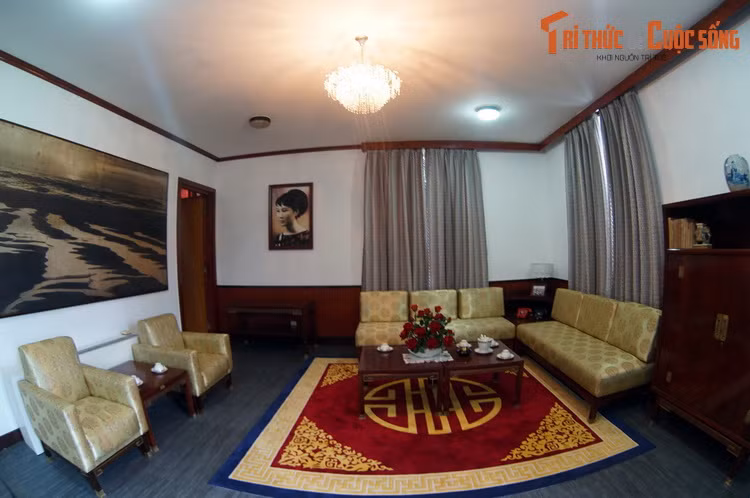 Bên trái căn phòng là nơi tiếp khách với các bộ bàn ghế sofa bọc vải vàng. Bức tường bên trái có bức ảnh khổ lớn về bãi biển miền Trung.