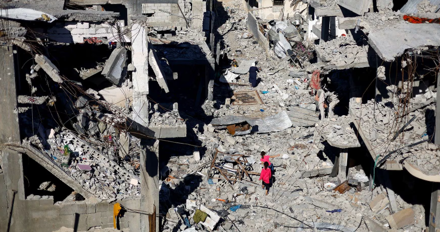 Các em nhỏ Palestine đi giữa những ngôi nhà bị phá hủy tại Khan Younis, phía nam Dải Gaza, hôm 19/11.