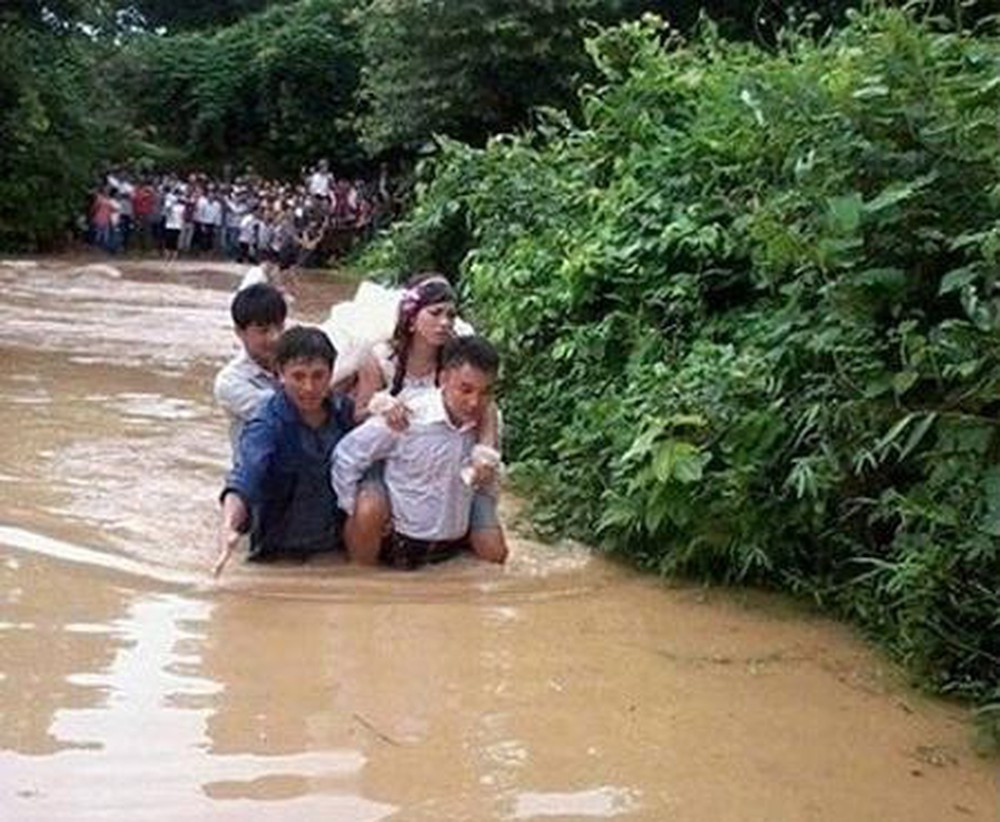 Ở một đám cưới khác, chú rể cúi đầu cõng cô dâu đi vì nước ngập khá cao.