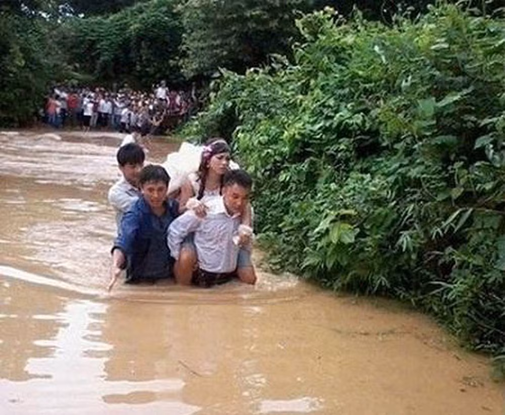 Ở một đám cưới khác, chú rể cúi đầu cõng cô dâu đi vì nước ngập khá cao.