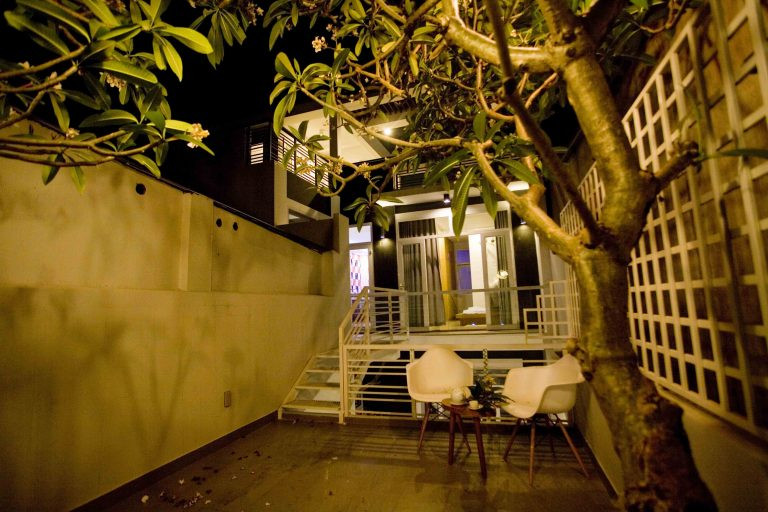 Một bộ bàn ghế nhỏ đặt dưới tán cây hoa rực rỡ trở thành nơi thư giãn lý tưởng cho gia đình.