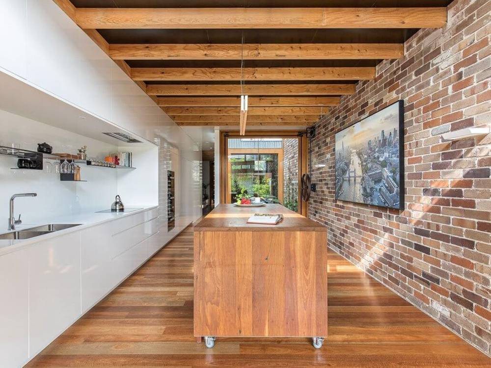 Tủ bếp hiện đại nổi bật trên nền sàn gỗ và tường gạch mộc.