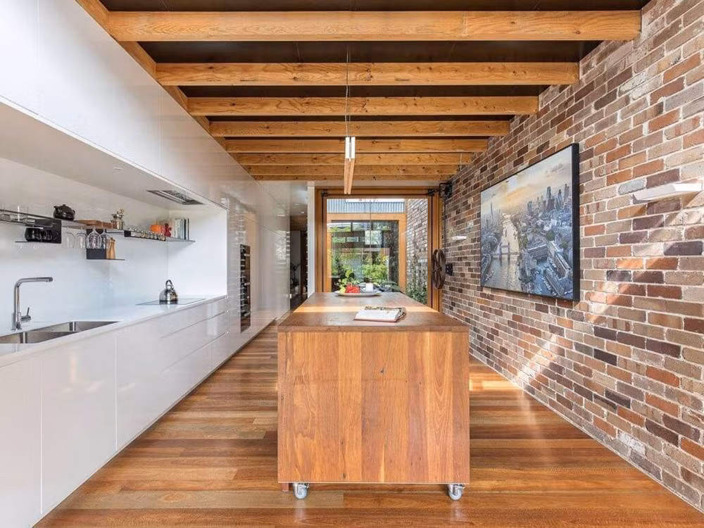 Tủ bếp hiện đại nổi bật trên nền sàn gỗ và tường gạch mộc.