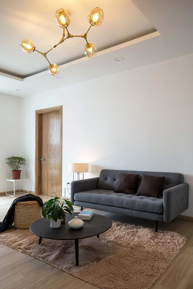 Phòng khách giản dị với sofa đơn, bàn trà tròn, thảm trải sàn và ghế ngồi làm thủ công.