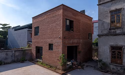 Ngôi nhà xây hình lập phương, bao quanh là những viên gạch đỏ thô.