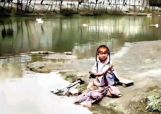 Một bé trai nhỏ tuổi phụ giúp gia đình giặt quần áo bên bờ sông.