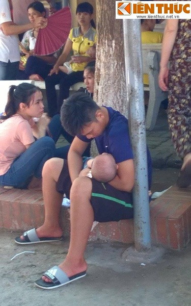 Ông bố bế con mới được vài tháng tuổi ngủ gục ở sân bệnh viện, dưới trời nắng trong khi chờ đợi tới lượt vào khám bệnh.