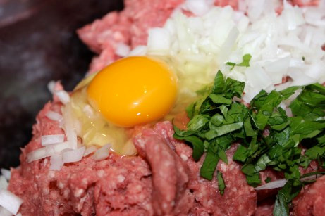 Cho thịt bò xay vào một cái bát thật to, lần lượt cho hành tây, rau mùi tây, tỏi băm, 2 quả trứng, nước khoáng, vụn bánh mì vào.