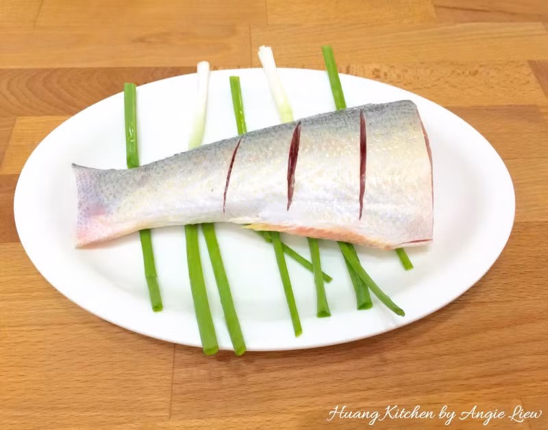 Cho cá ra đĩa hấp, lót vài cọng hành tươi bên dưới rồi đặt cá lên.