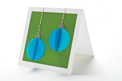 Thiệp Giáng sinh 3D: Cắt 2 hình tròn bằng giấy, gấp đôi một hình tròn lại rồi dán đè lên hình tròn còn lại, chỉ dán một nửa để tạo thành một hình cầu 3D. Xâu chỉ và gắn lên một miếng bìa là bé đã có một tấm thiệp Giáng sinh thủ công giành tặng bạn bè và người thân. 