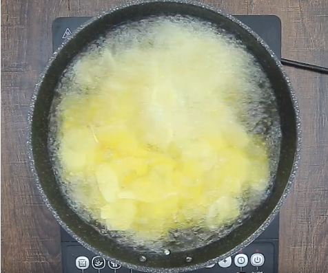 Đổ dầu ngập chảo đun sôi rồi cho khoai tây vào, Vừa chiên vừa đảo để khoai vàng đều.