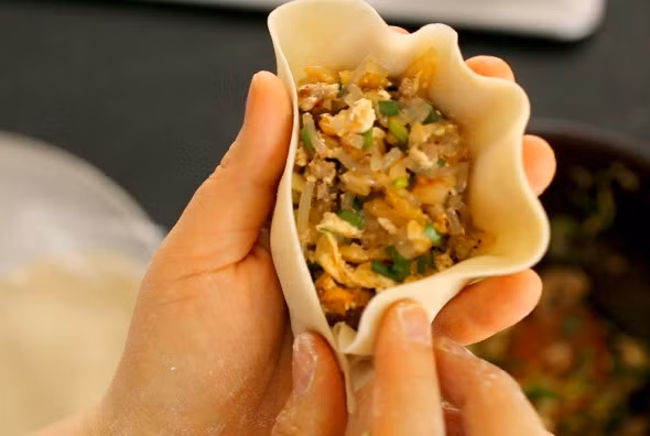 Đặt vỏ bánh vào lòng bàn tay rồi dùng thìa xúc nhân cho vào giữa.