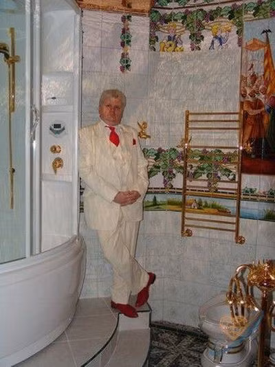 Khuôn mặt béo tròn trong trang phục comple trắng toát bên cạnh chiếc giá treo khăn tắm bằng vàng.