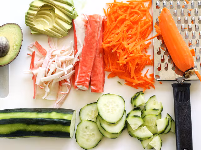 Các nguyên liệu xếp lên trên món sushi ăn trong bát gồm bơ, dưa chuột, cà rốt và thanh cua. 