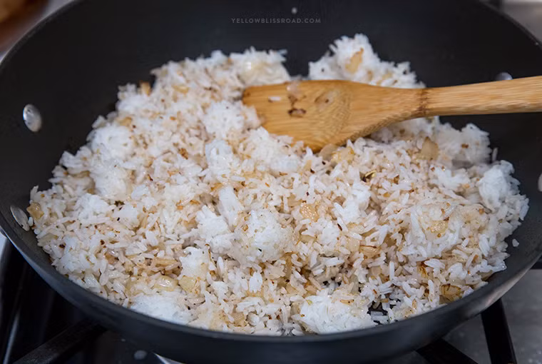 Cho cơm nguội vào đảo cùng với hành tây cho thơm đến khi cơm nóng đều.