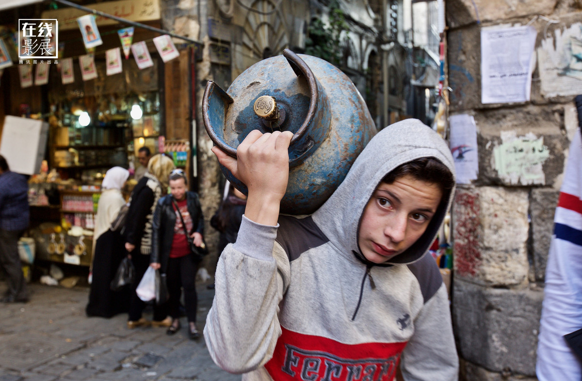 Nam thiếu niên đang vác bình ga trên đường phố Damascus.