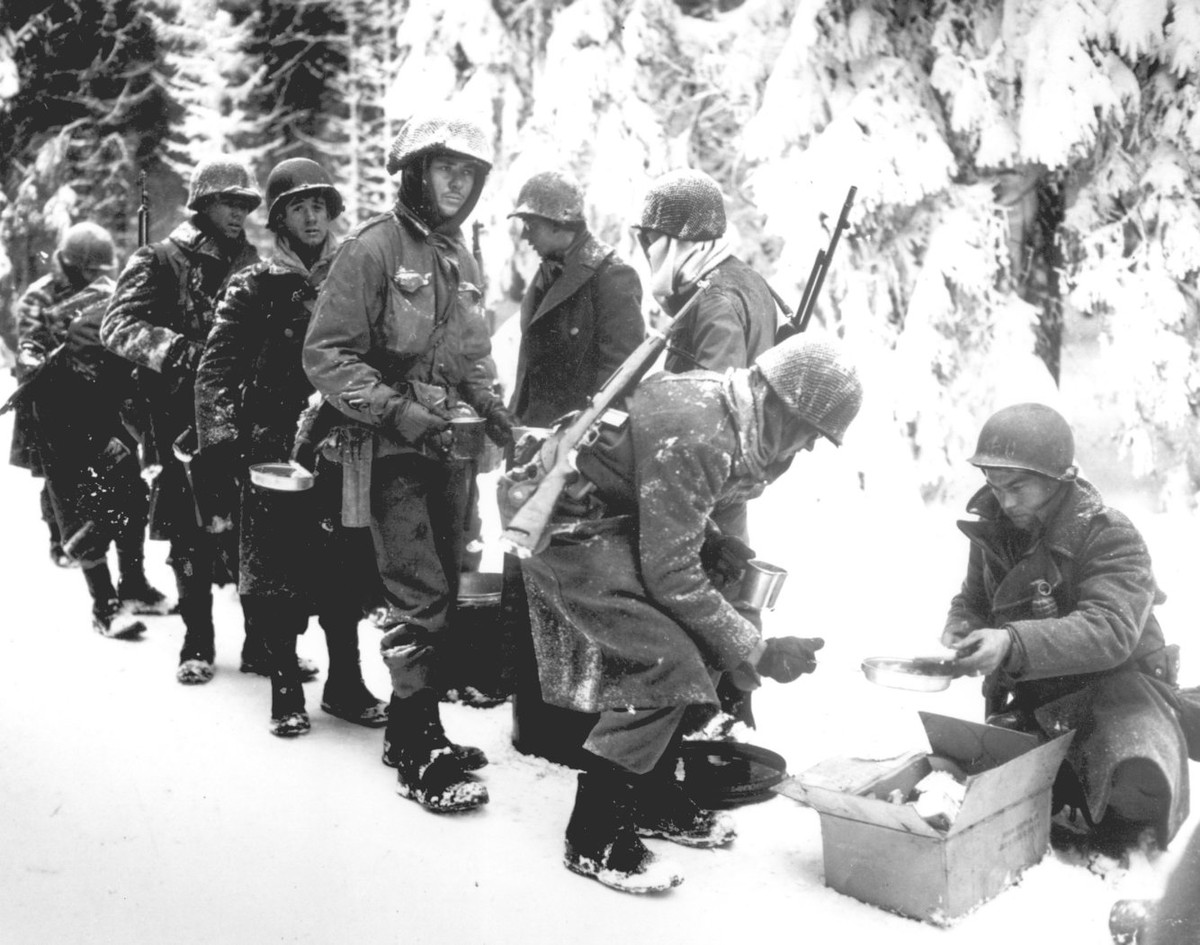 Binh lính Mỹ trong trận Bulge chia khẩu phần ăn sau khi nhận được hàng tiếp tế từ được lực lượng không quân mang tới. Nguồn ảnh: BI.