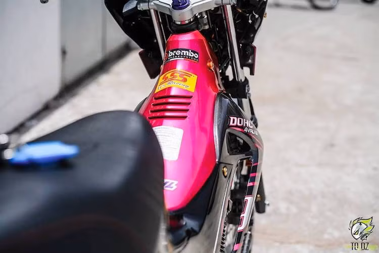 Bên cạnh phần đầu "mắt phượng, một điểm độc đáo của thế hệ Satria 150 này đó là phiên bản màu sắc hồng/đen cá tính. Khi dọn mới lại chiếc xe, chủ xe đã lựa chọn bản màu "ít đụng hàng" này. Ngoài ra, bộ yên với đệm mút mỏng và áo yên vân tương tự xe số Honda Dream II "huyền thoại" cũng khiến chiếc xe nổi bật hơn.