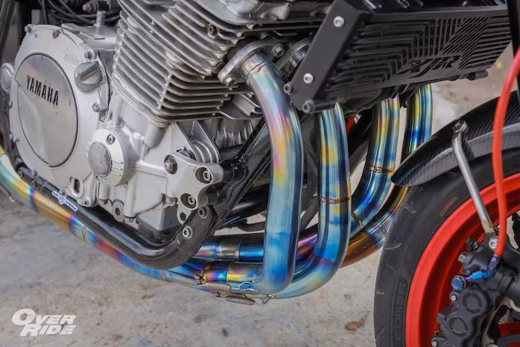 Trên bản độ này, chủ xe đã cập nhật nhẹ động cơ bằng cách độ lọc gió K&amp;N, tinh chỉnh chế hòa khí và độ hệ thống xả titan. Cây pô Termignoni carbon lấy từ xe Ducati không chỉ khiến XJR1300 "thoáng máy" hơn mà còn khiến tiếng "hú" đặc trưng của động cơ 4 xi-lanh trở nên to và rõ ràng hơn.