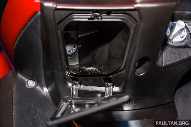 Ở phía dưới phần đầu, NVX 155 có một hộc chứa đồ nhỏ được tích hợp cổng sạc 12V để sạc các thiết bị di động khi xe di chuyển. Tuy nhiên, phần nắp đậy bằng nhựa chỉ được giữ bằng các ngàm nhựa nhỏ không chắc chắn, chính vì vậy người dùng phải lưu ý cầm theo điện thoại khi dừng xe.