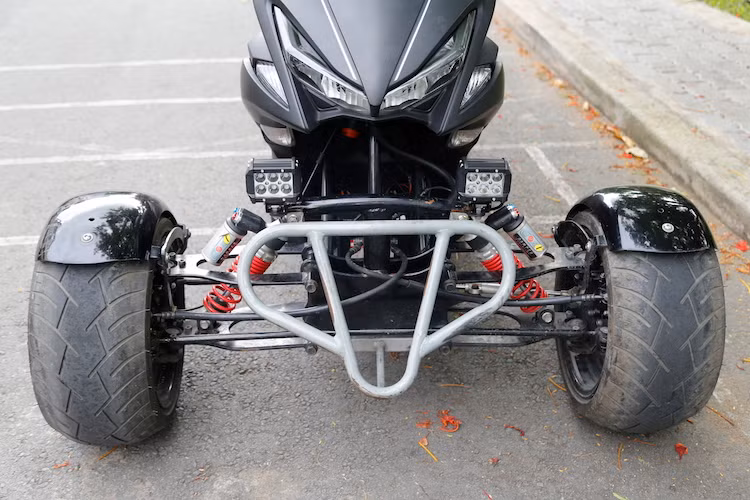 Trên bản độ này, bánh trước của chiếc NVX nguyên bản cùng hệ thống phuộc đã bị loại bỏ, thay vào đó là cặp bánh kép theo phong cách các dòng xe Can-Am. Để có thể độ bánh trước kép, xưởng độ đã phải thiết kế ra một hệ thống khung đỡ tương tự như xe hơi cho chiếc NVX.