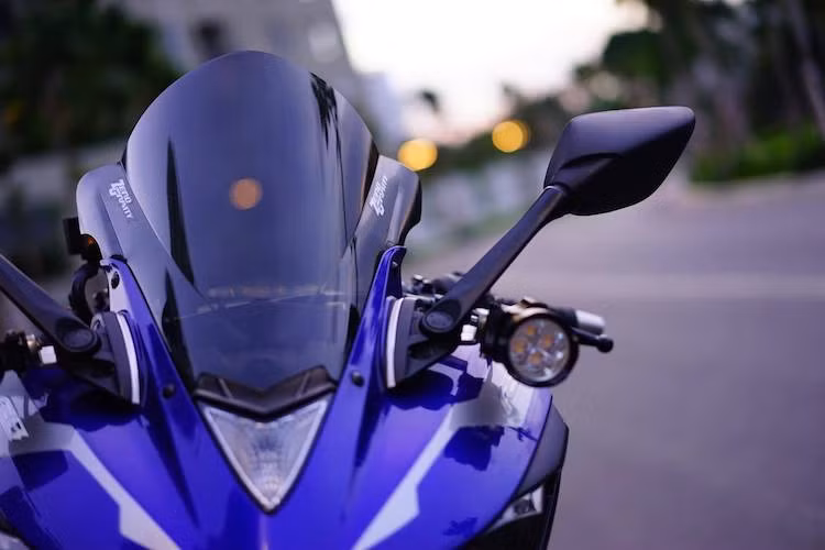 Ở phía trước, chiếc kính chắn gió nguyên bản của R3 đã được chủ nhân thay bằng kính độ của hãng Zero Gravity, đem tới độ cản gió tốt hơn. Nằm hai bên chân gương chiếu hậu là cặp đèn LED L4 với pad gọn gàng, bổ sung độ sáng cho đèn pha nguyên bản trong đêm tối.