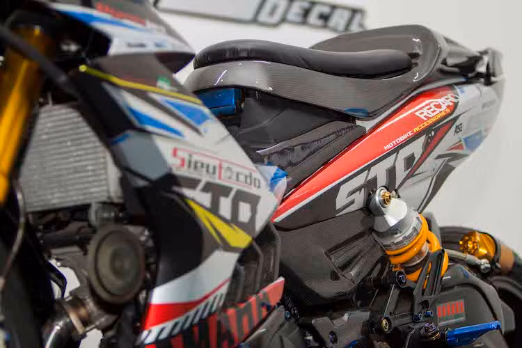 Toàn bộ dàn vỏ nguyên bản của chiếc Exciter cũng có sự thay đổi là được dán sợi carbon thật sau đó phủ bóng. Chưa dừng lại ở đó, một bộ tem trên chất liệu decal candy cũng khiến cho chiếc xe trông nổi bật và bắt mắt hơn. Theo phong cách xe đua, bộ yên nguyên bản của Exciter cũng đã được chế lại với đệm mỏng và yên solo.