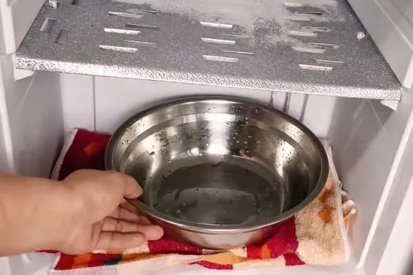 Bước 2, chuẩn bị 1 chiếc khăn khô và chiếc bát lớn. Dùng chiếc khăn lót đều dưới bề mặt ngăn đông. Đặt bát lên trên chiếc khăn rồi đổ nước nóng vào. Đóng cửa tủ lạnh và đợi khoảng 10 -20 phút. Lúc này, chiếc khăn lót vừa dùng để thấm nước khi đá tan, vừa có ý nghĩa bảo vệ các kệ trong ngăn đông, tránh tiếp xúc trực tiếp với đáy bát nóng.