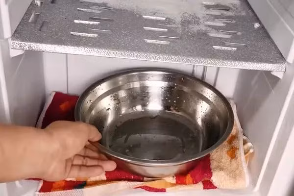 Bước 2, chuẩn bị 1 chiếc khăn khô và chiếc bát lớn. Dùng chiếc khăn lót đều dưới bề mặt ngăn đông. Đặt bát lên trên chiếc khăn rồi đổ nước nóng vào. Đóng cửa tủ lạnh và đợi khoảng 10 -20 phút. Lúc này, chiếc khăn lót vừa dùng để thấm nước khi đá tan, vừa có ý nghĩa bảo vệ các kệ trong ngăn đông, tránh tiếp xúc trực tiếp với đáy bát nóng.