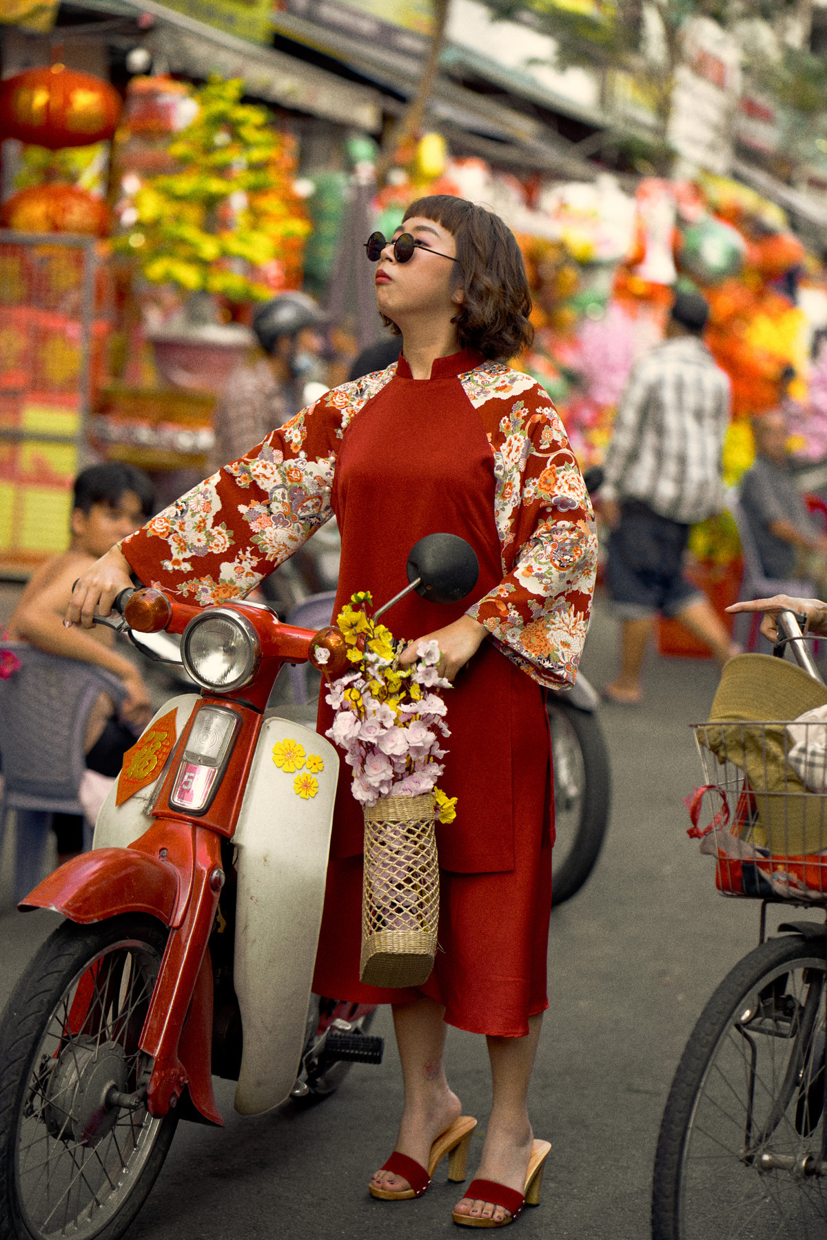 Trang Hý trong tà áo dài cách tân sành điệu và chiếc Honda Cub gợi nhớ không khí tết miền Nam thập niên 90. Cô đi dọc “phố tài lộc” Hải Thượng Lãn Ông và chợ Bình Tây với biểu cảm đáng yêu.